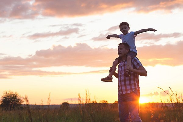 Father carrying his son on his shoulders with sunset behind them