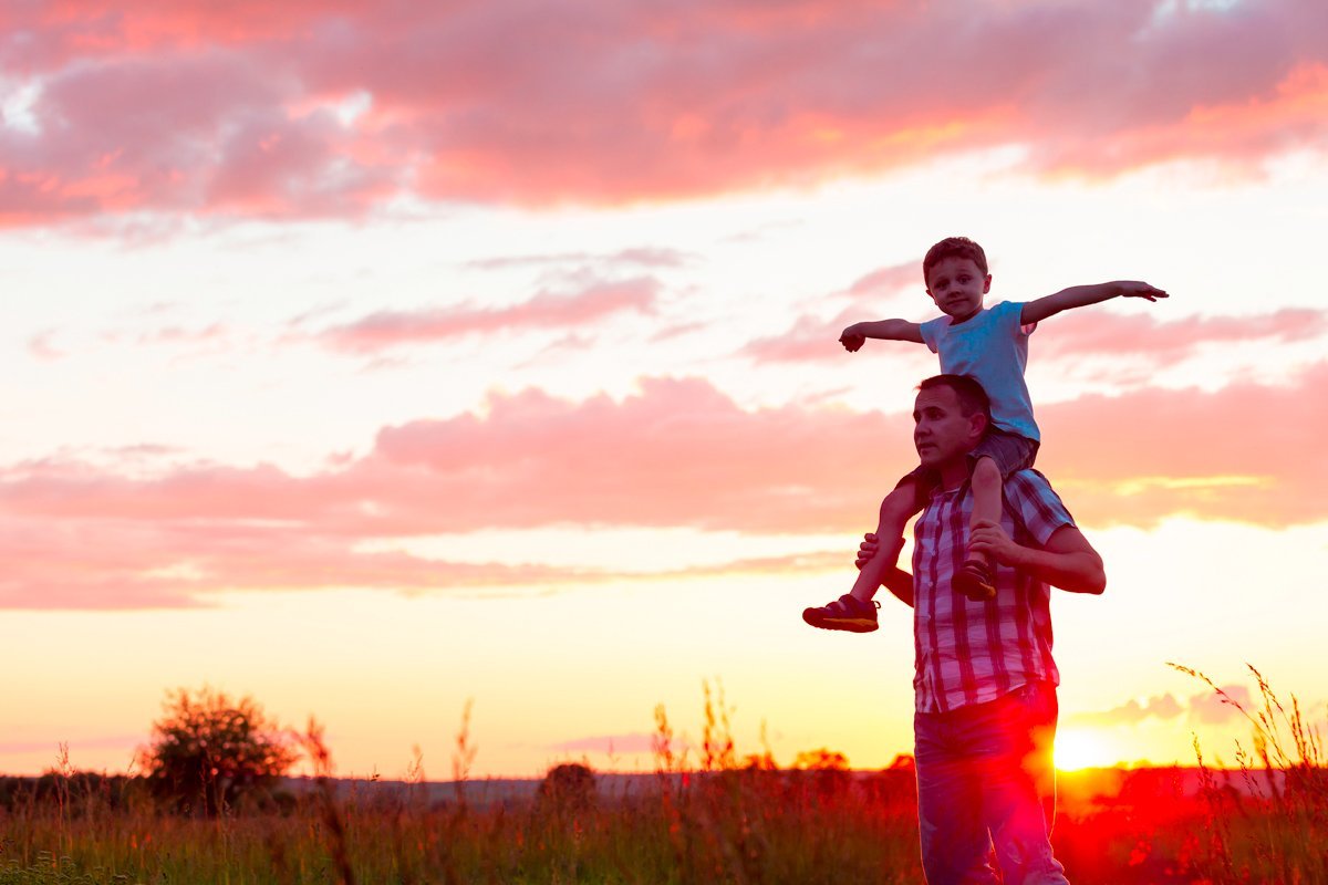 Father carrying his son on his shoulders with sunset behind them