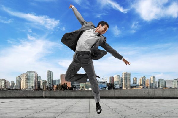 A businessman jumping exuberantly outdoors in downtown Vancouver on a beautiful sunny day