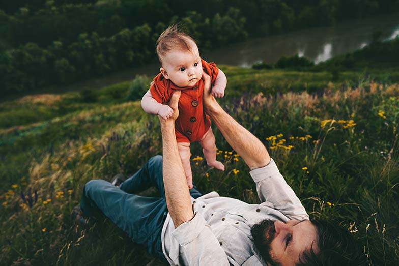 Dad lying on the grass lifting his baby