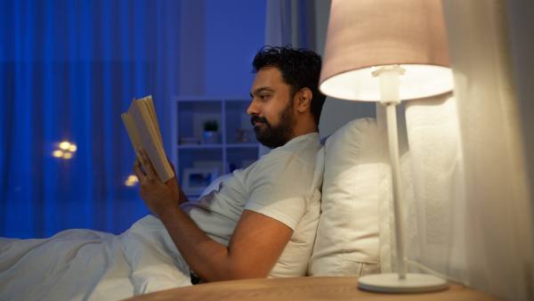 Man in bed at night reading with lamp turned on