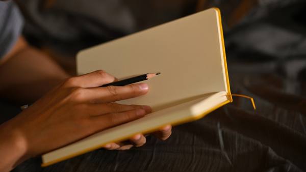 Two hands holding a journal and a pencil