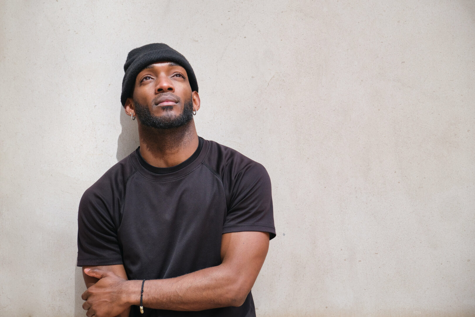 Young african american man with a beanie is posing in front of a white wall, looking up