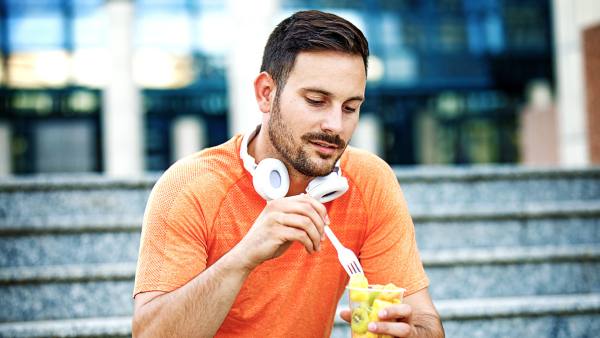 Man in orange shirt wearing white headphones and eating fruit