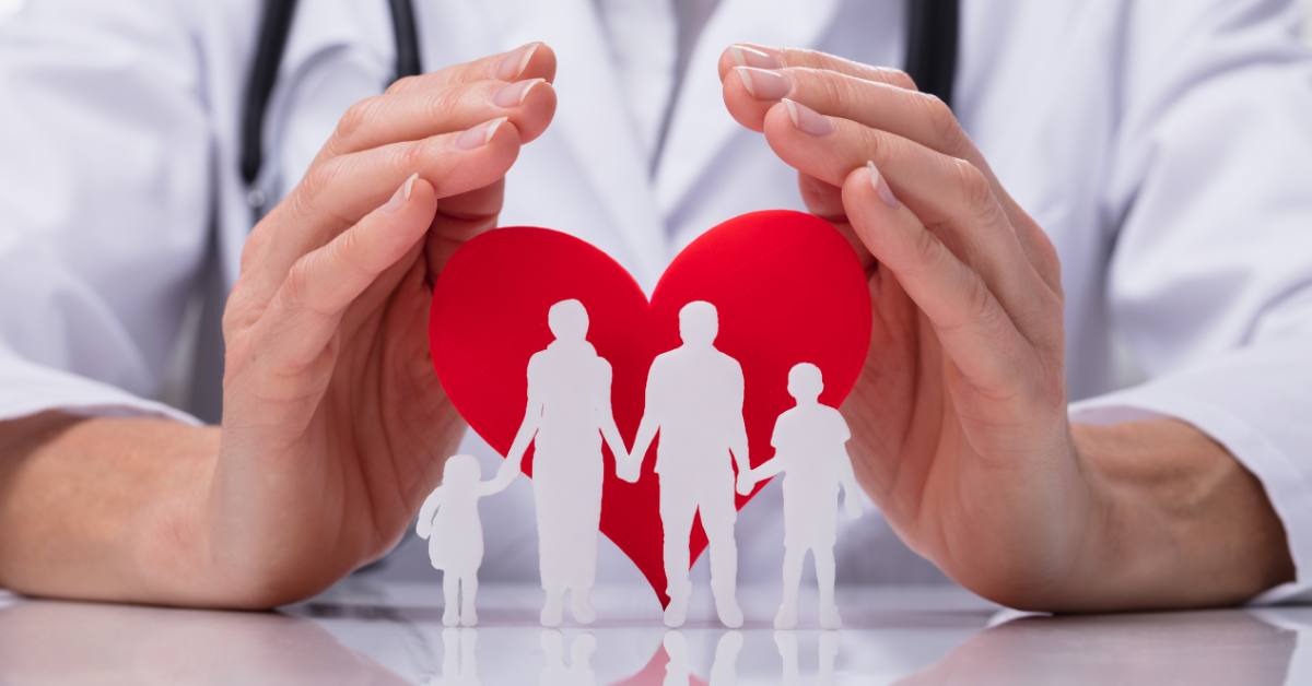 Doctor's hands holding a red heart and silhouette of a family