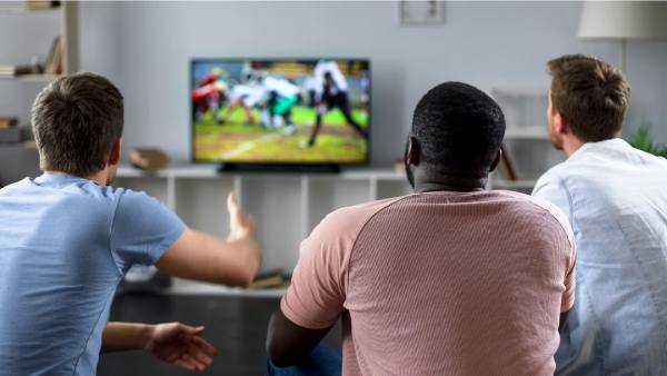 Three men sitting watching sports on tv
