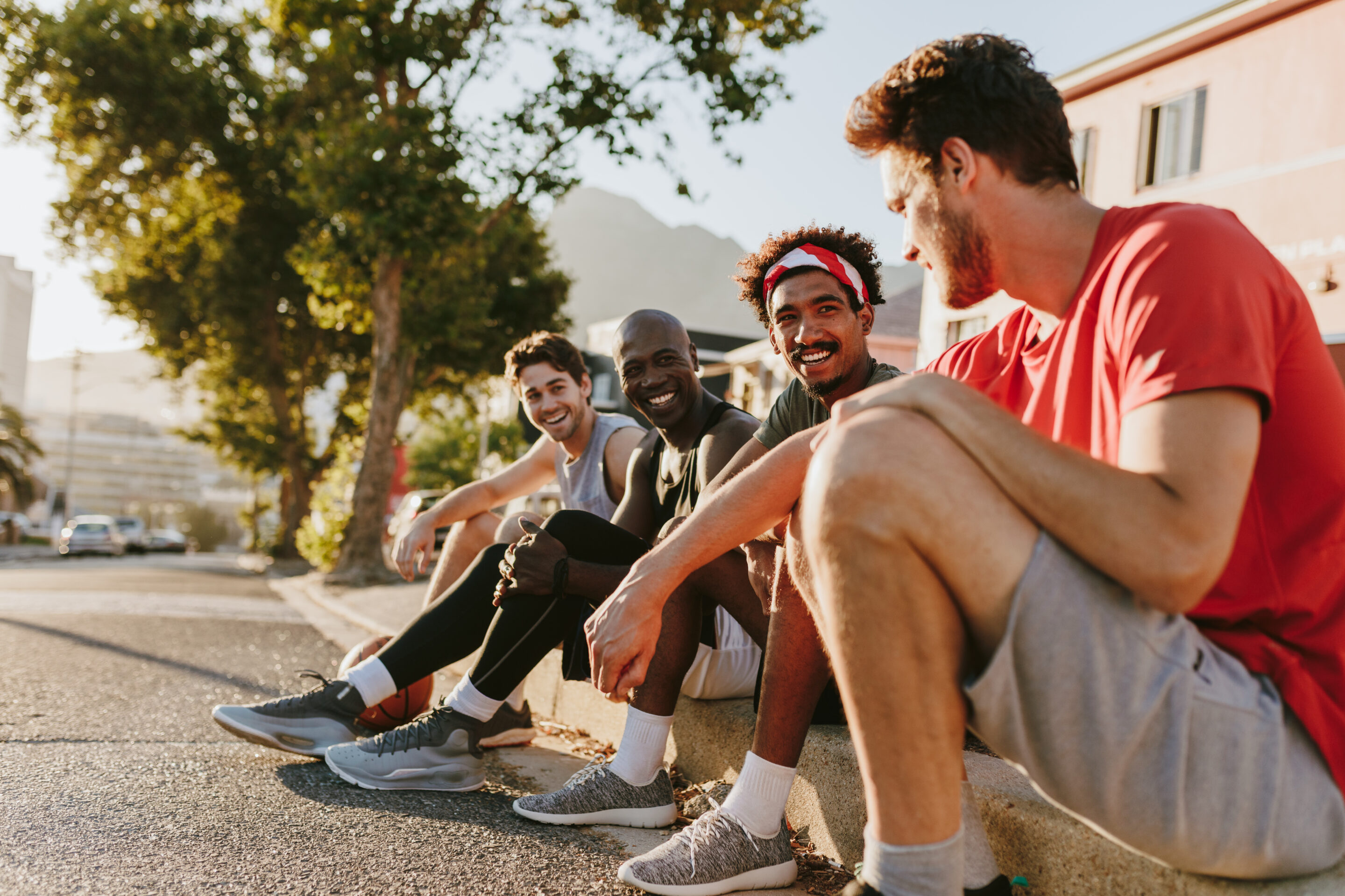 guys relaxing on a curb after playing basketball